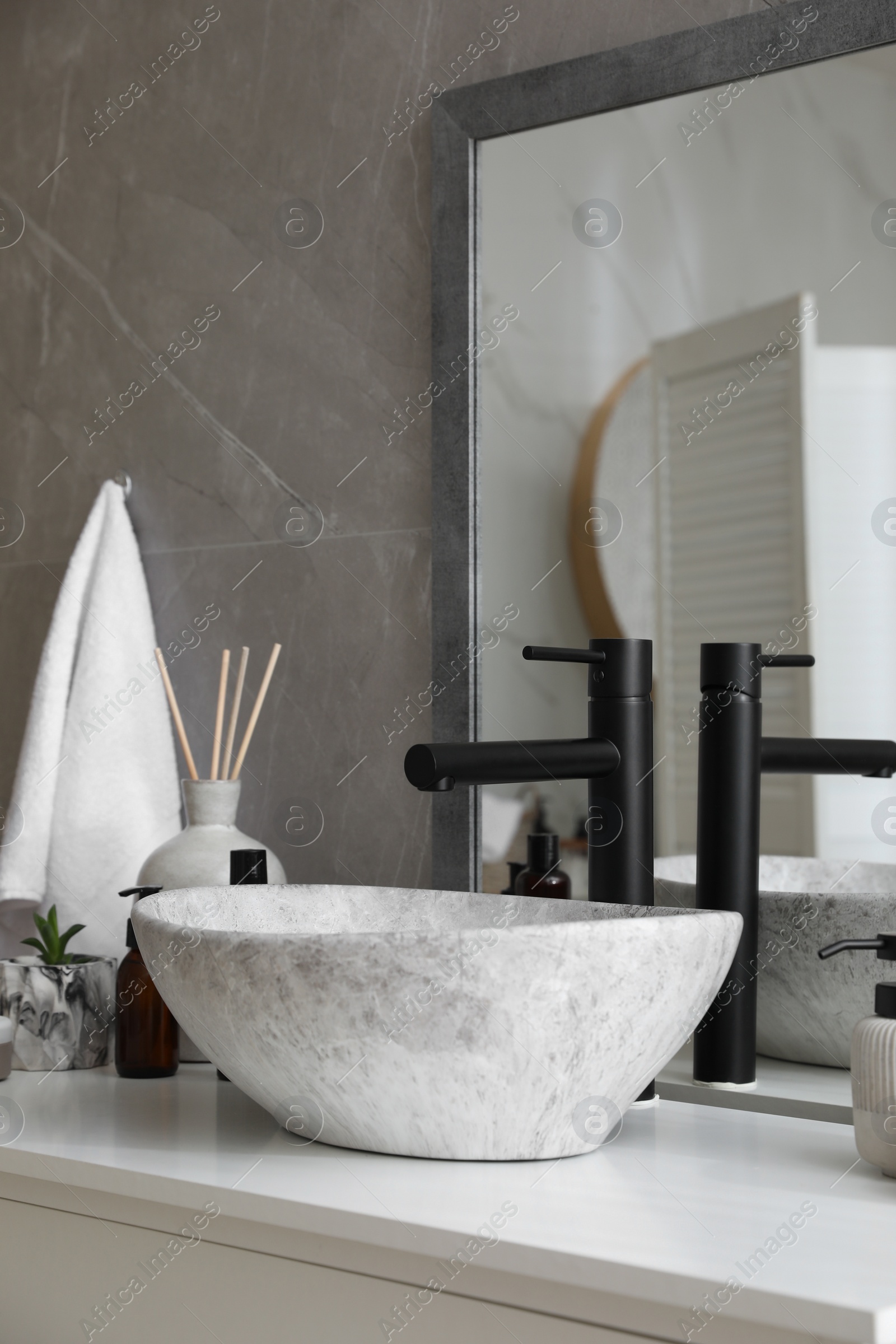 Photo of Stone vessel sink with faucet and toiletries on white countertop in bathroom