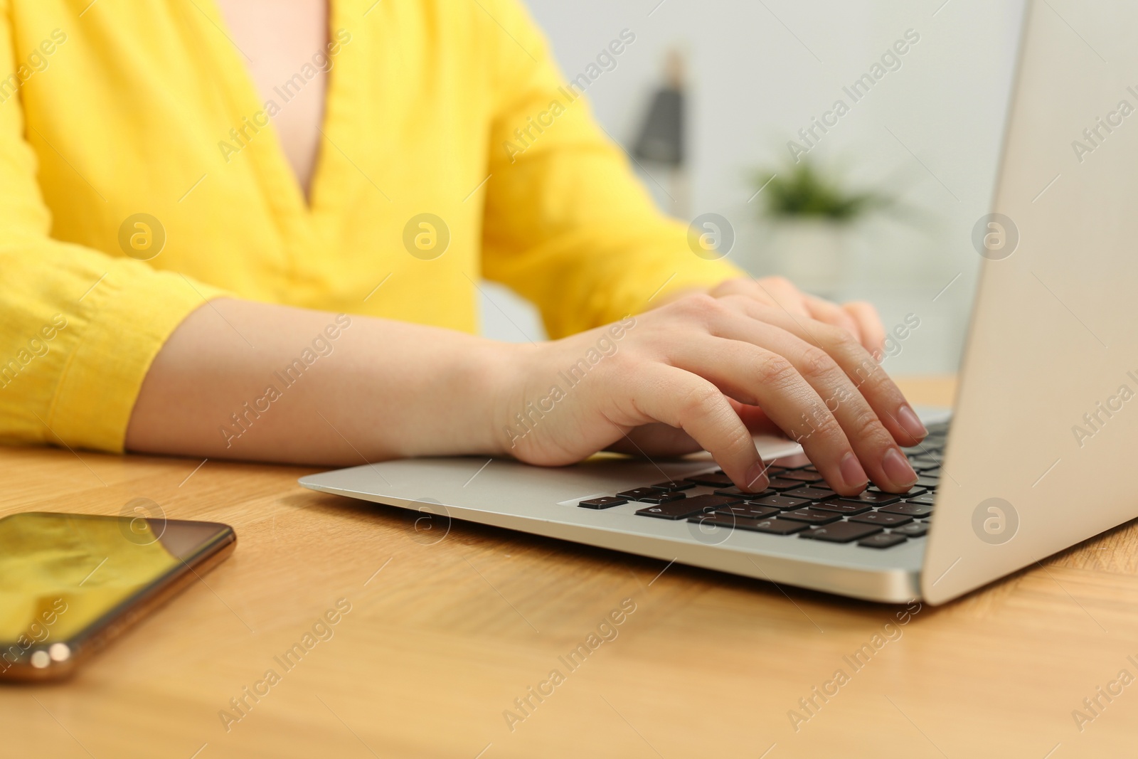 Photo of Home workplace. Woman working on laptop at wooden desk indoors, closeup