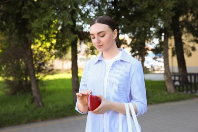 Photo of Young woman holding purse with banknotes outdoors