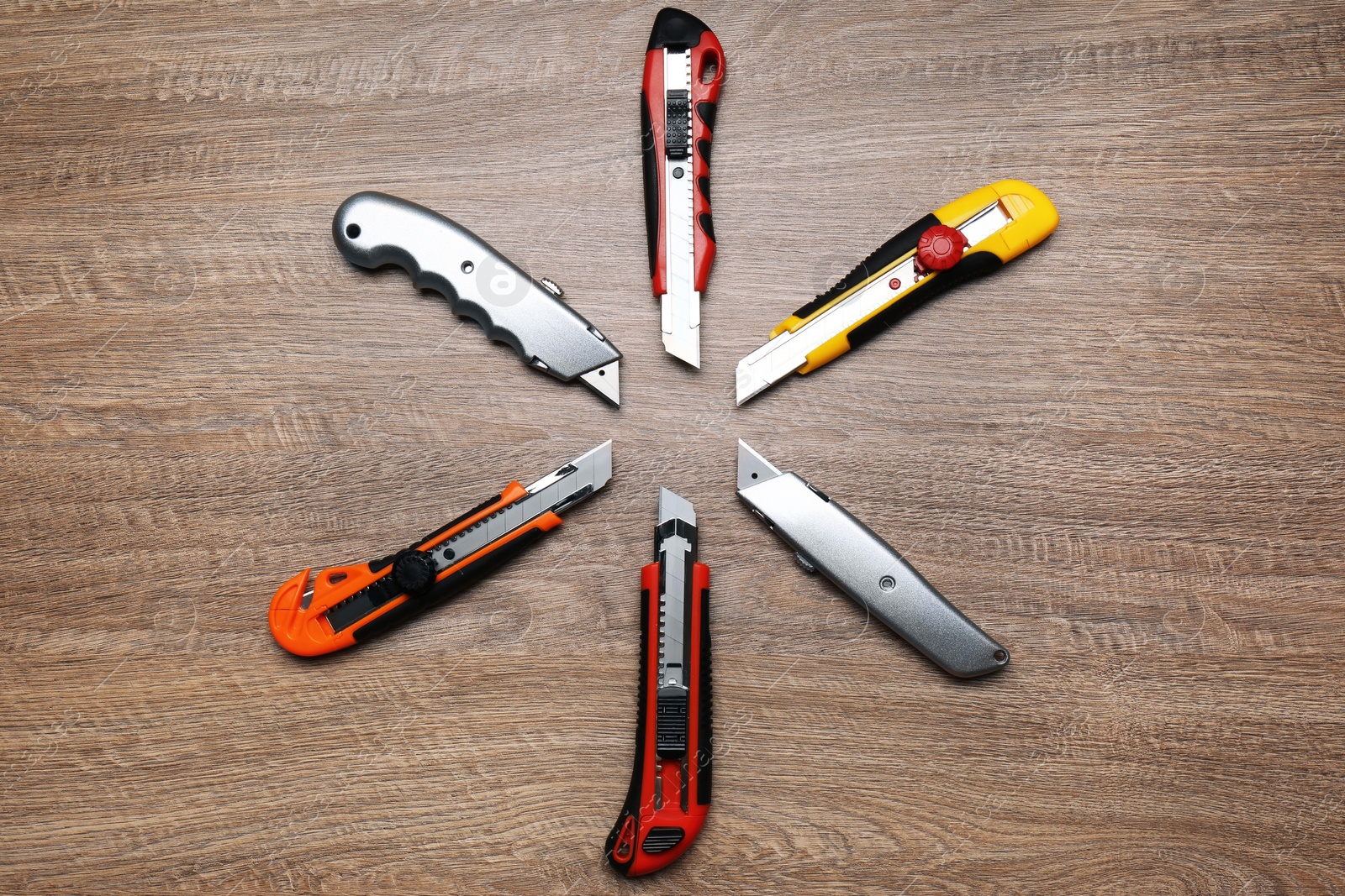 Photo of Many different utility knives on wooden table, flat lay