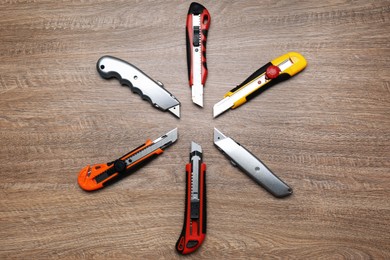 Photo of Many different utility knives on wooden table, flat lay