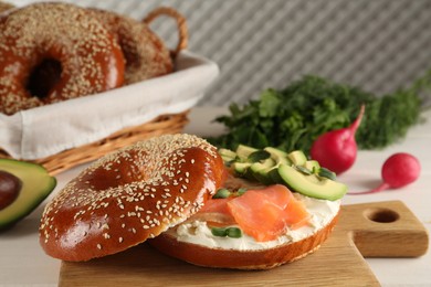 Photo of Delicious bagel with cream cheese, salmon, avocado and microgreens on wooden board