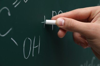 Teacher writing chemical formulas with chalk on green chalkboard, closeup