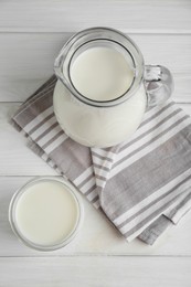 Photo of Jug and glass of fresh milk on white wooden table, flat lay