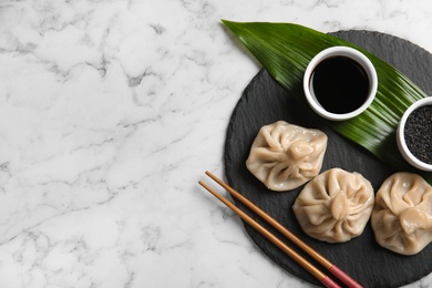 Photo of Slate plate with tasty baozi dumplings, chopsticks, sesame seeds and soy sauce on marble table, top view. Space for text