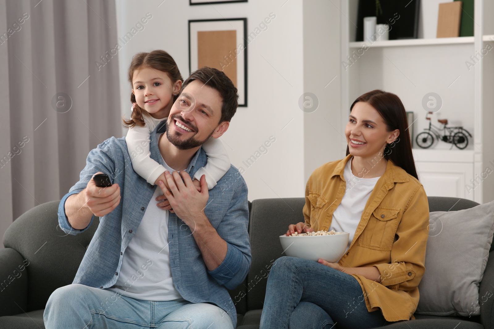 Photo of Happy family watching movie at home. Father changing TV channels with remote control