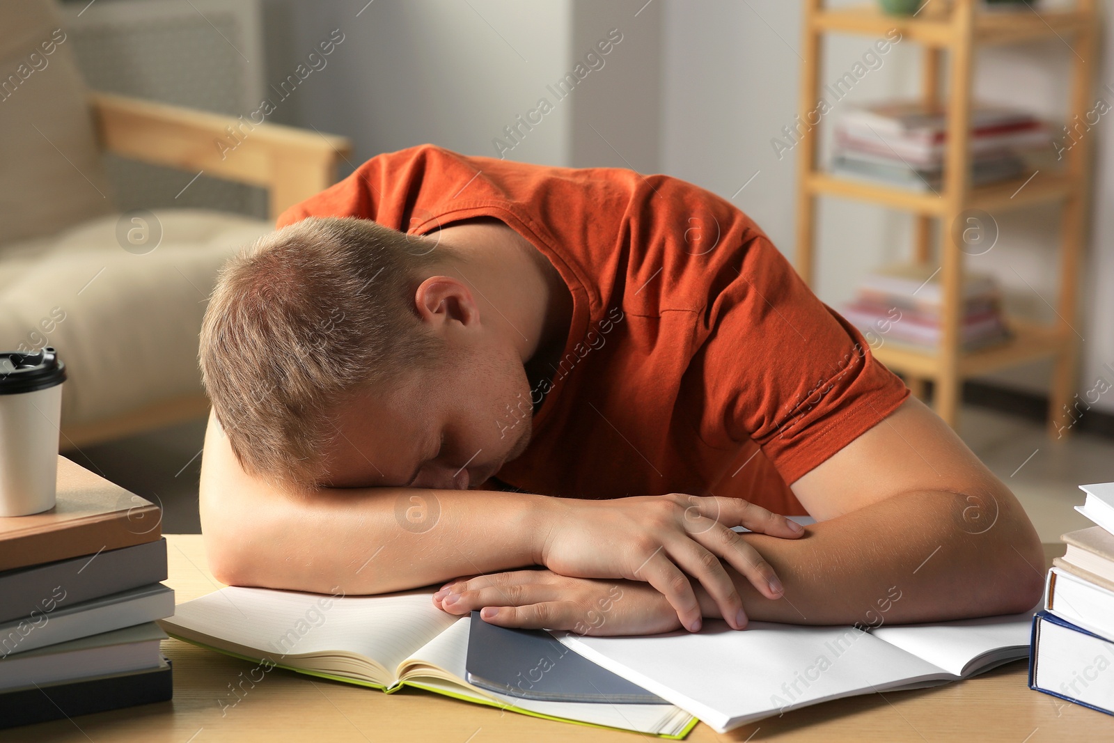 Photo of Tired man sleeping near books at wooden table indoors