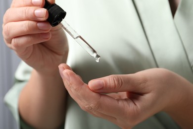 Photo of Woman applying cosmetic serum onto hand on blurred background, closeup