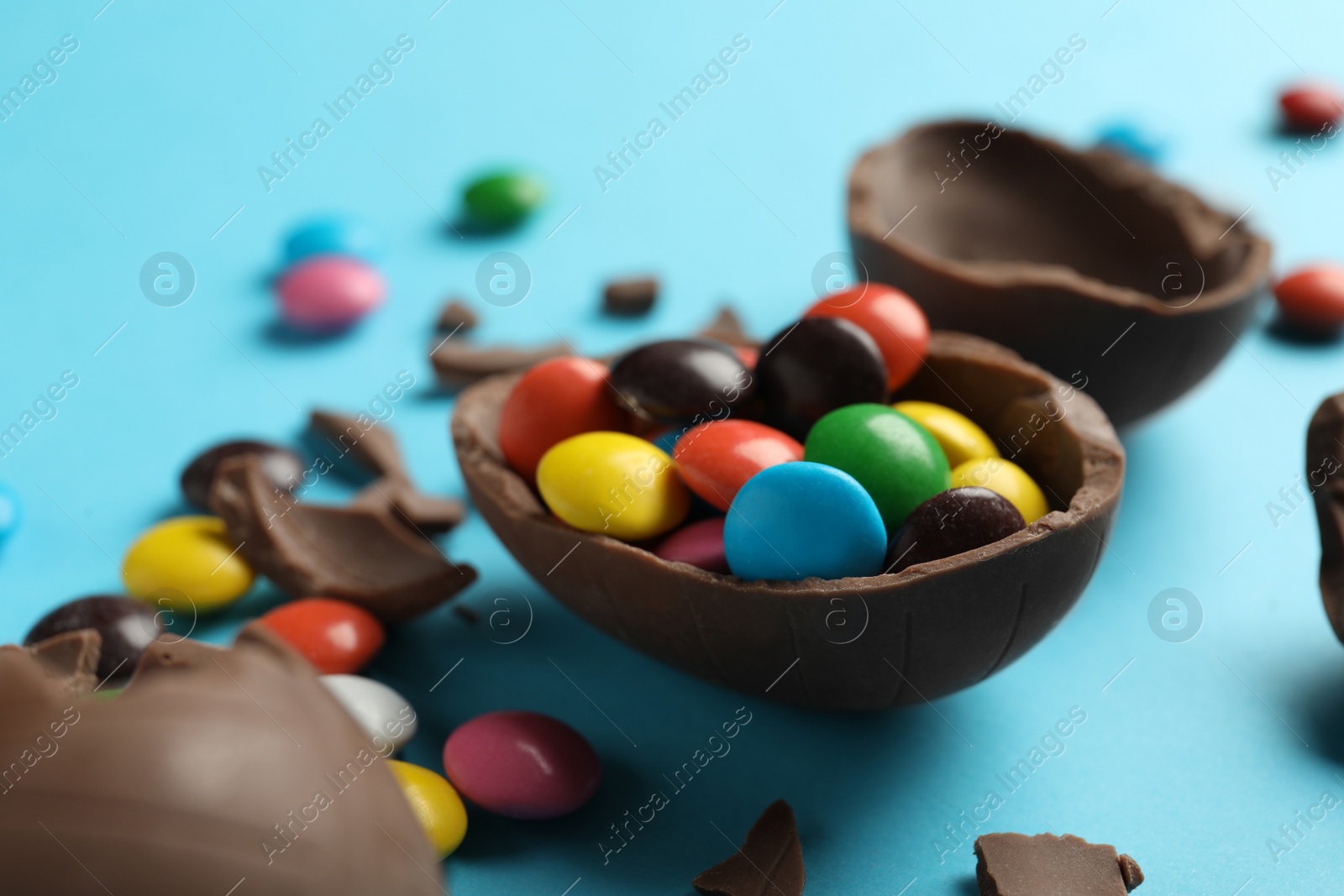 Photo of Broken chocolate eggs with candies on light blue background, closeup