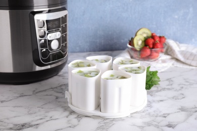 Photo of Cups of homemade fruit yogurt near multi cooker on marble table