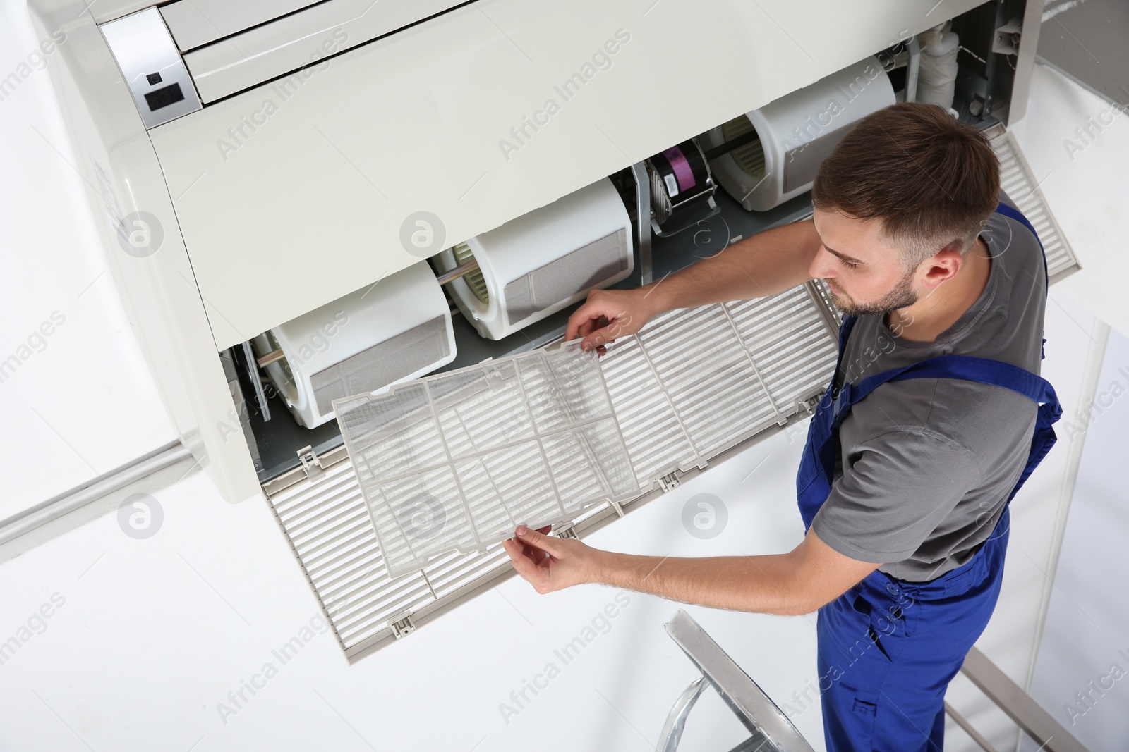 Photo of Young male technician cleaning air conditioner indoors