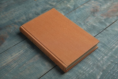 Photo of Hardcover book on light blue wooden table. Space for text