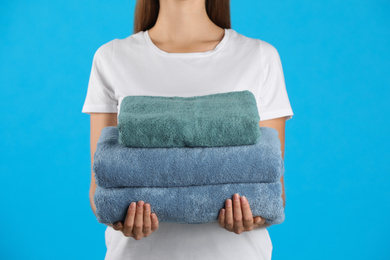 Woman holding fresh towels on light blue background, closeup