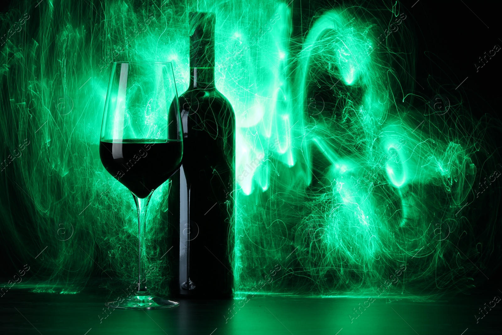 Photo of Red wine in glass and bottle in green lights, space for text