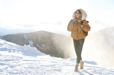 Happy young woman with backpack spending winter vacation in mountains. Space for text