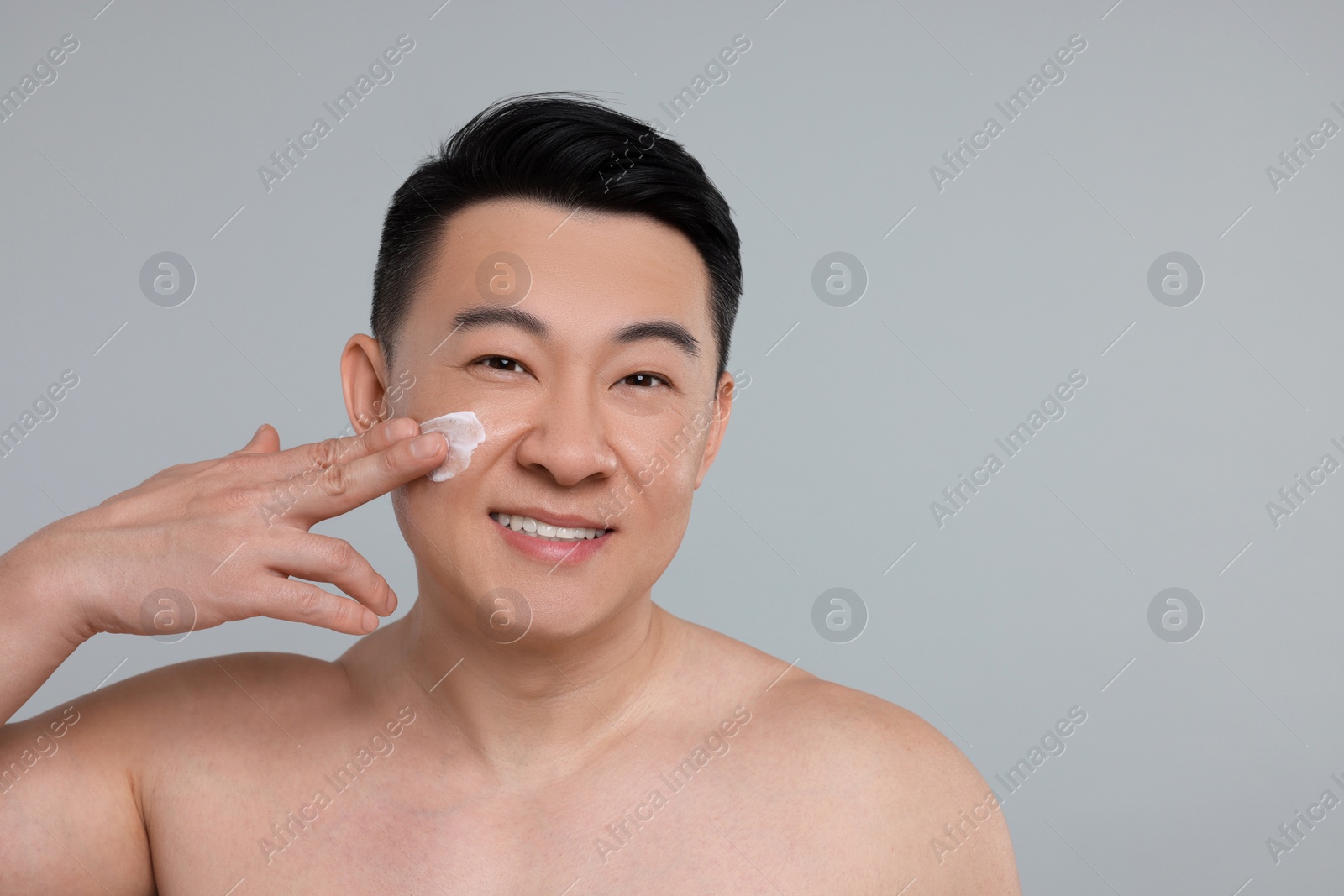 Photo of Handsome man applying cream onto his face on light grey background. Space for text