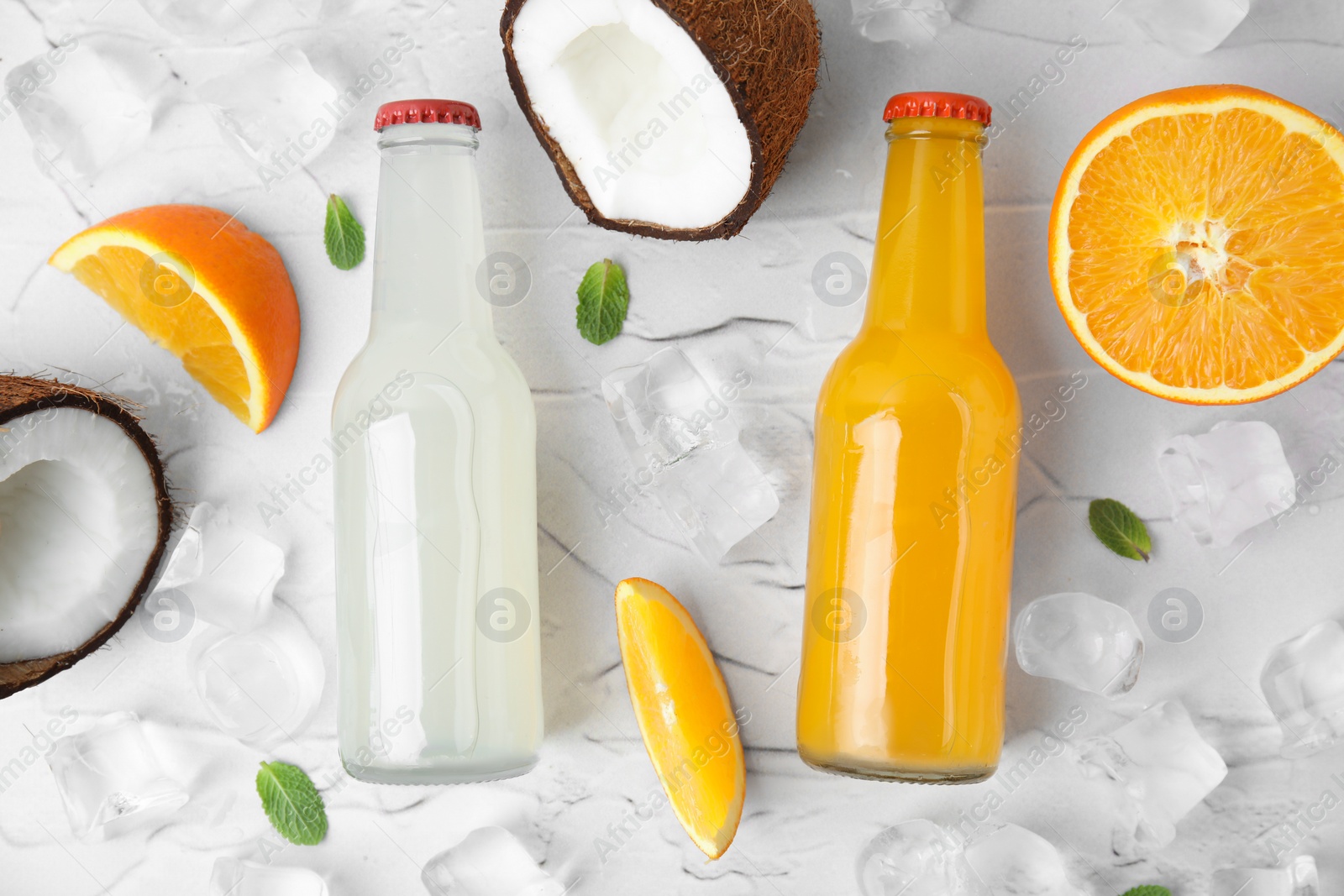 Photo of Tasty kombucha in glass bottles, fresh fruits and ice on white textured table, flat lay