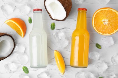 Tasty kombucha in glass bottles, fresh fruits and ice on white textured table, flat lay