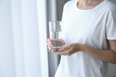 Woman holding glass of water near window at home, closeup