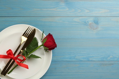 Beautiful table setting with red rose and space for text on light blue wooden background, top view. Valentine's Day dinner