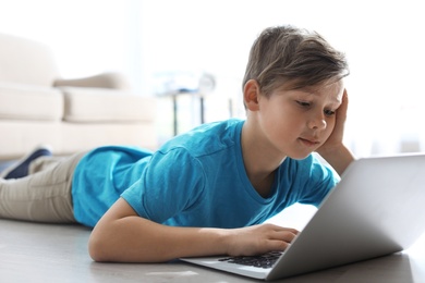 Photo of Little child with laptop on floor indoors. Danger of internet