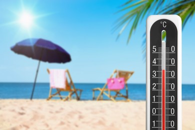 Image of Weather thermometer and beautiful sandy beach with wooden sunbeds on background. Heat stroke warning