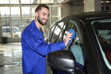 Worker cleaning automobile window with rag at car wash