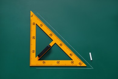 Photo of Yellow triangle and chalk on green chalkboard, flat lay