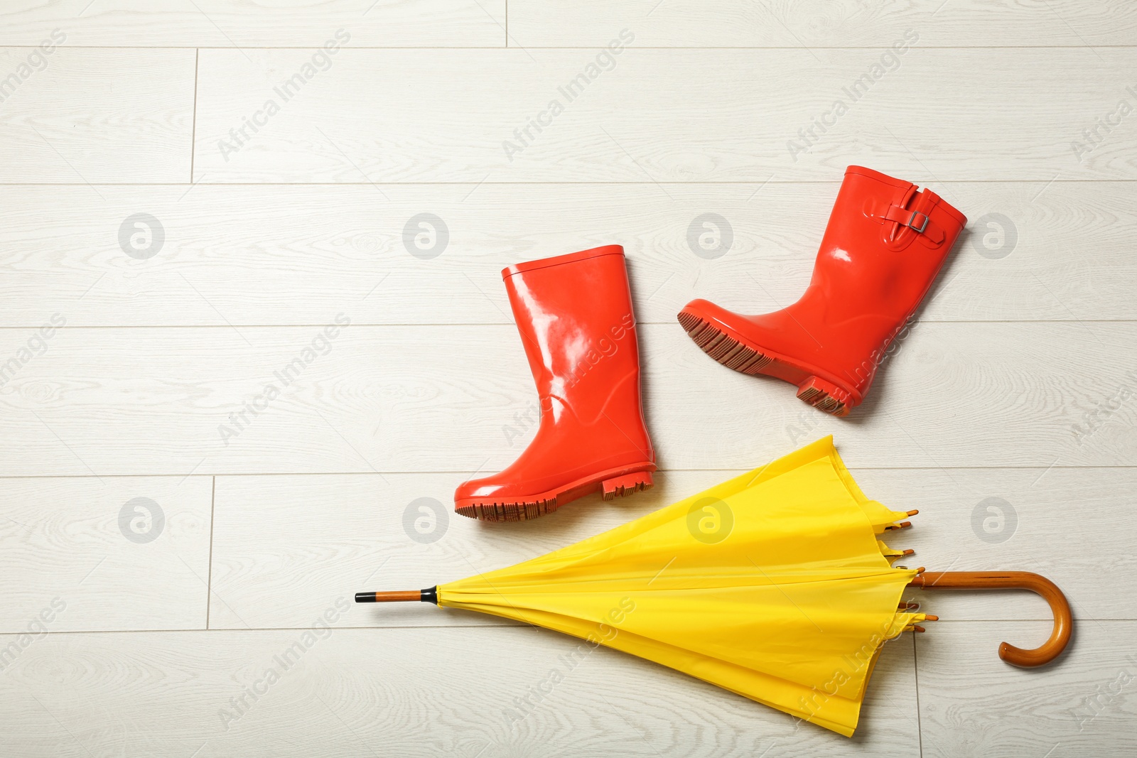 Photo of Color umbrella and rubber boots on wooden floor, flat lay. Space for text