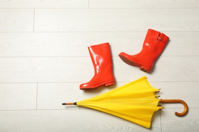 Photo of Color umbrella and rubber boots on wooden floor, flat lay. Space for text