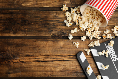 Photo of Tasty fresh pop corn and clapboard on wooden table, flat lay. Space for text