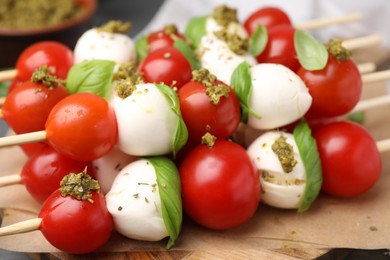 Photo of Caprese skewers with tomatoes, mozzarella balls, basil and pesto sauce on table, closeup