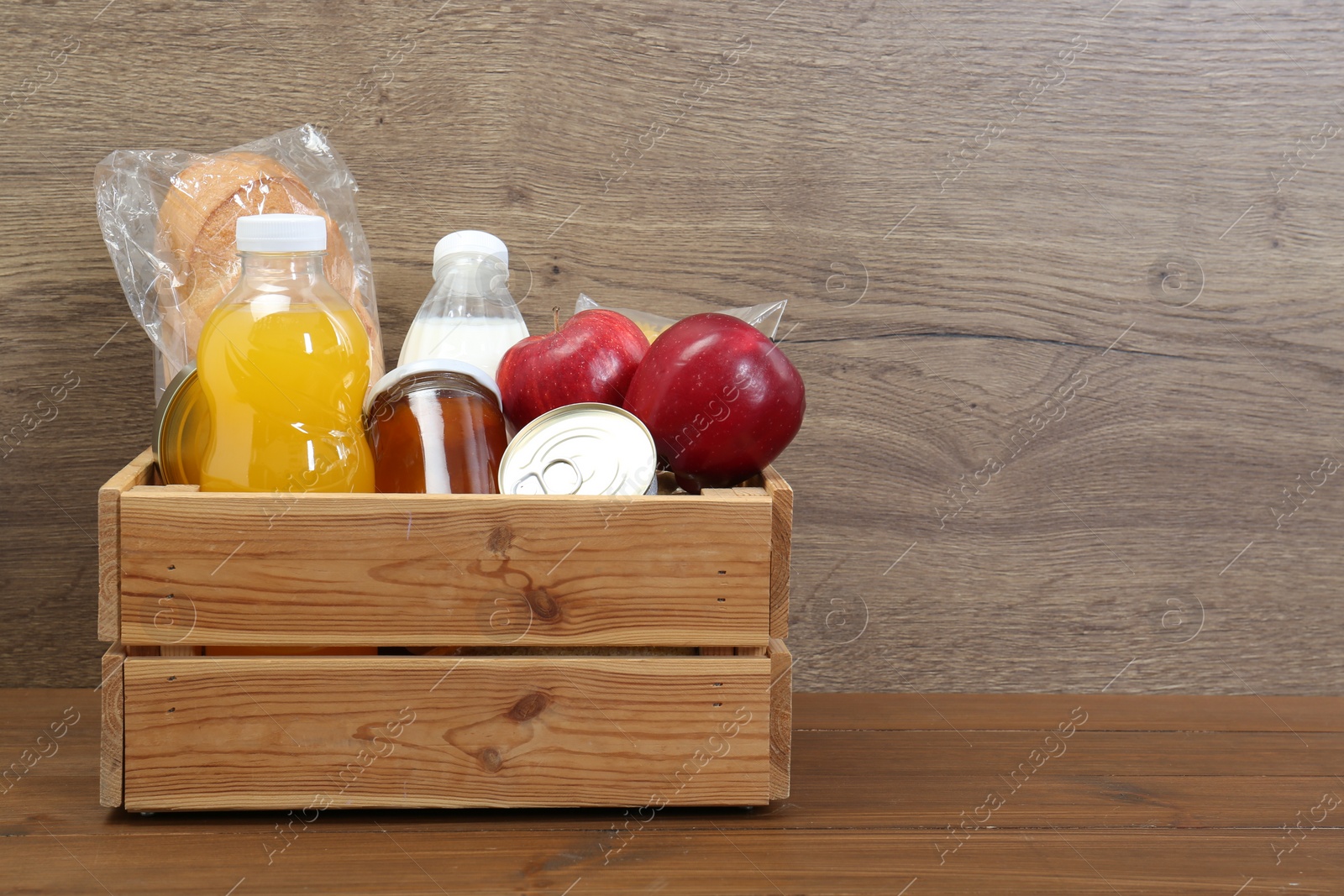 Photo of Humanitarian aid. Different food products for donation in crate on wooden table. Space for text