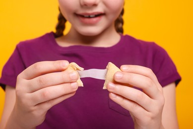 Girl holding tasty fortune cookie with prediction on orange background, closeup