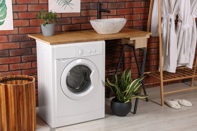 Washing machine and wooden rack with terry bathrobes indoors. Laundry room interior design