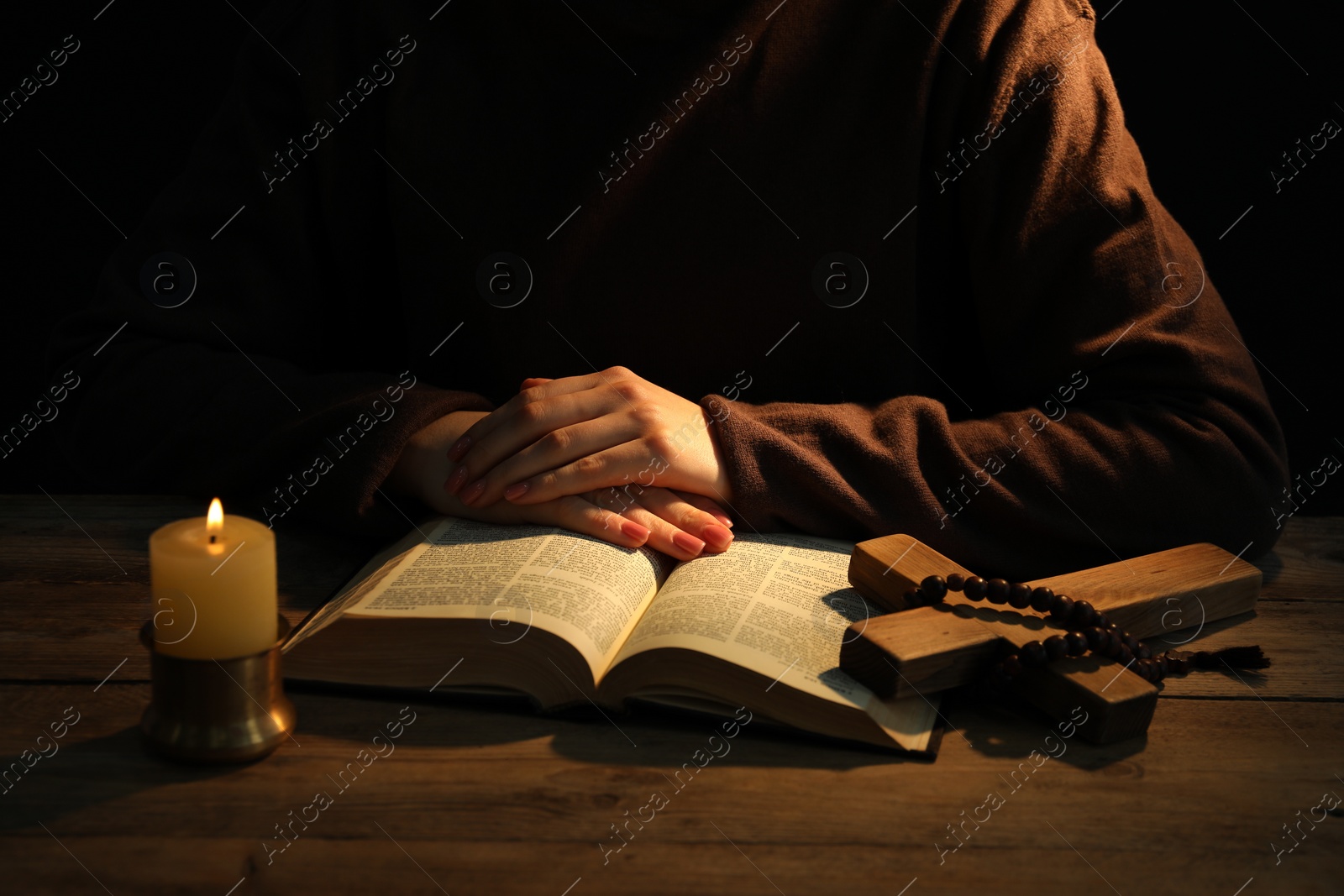 Photo of Woman praying at table with burning candle and Bible, closeup