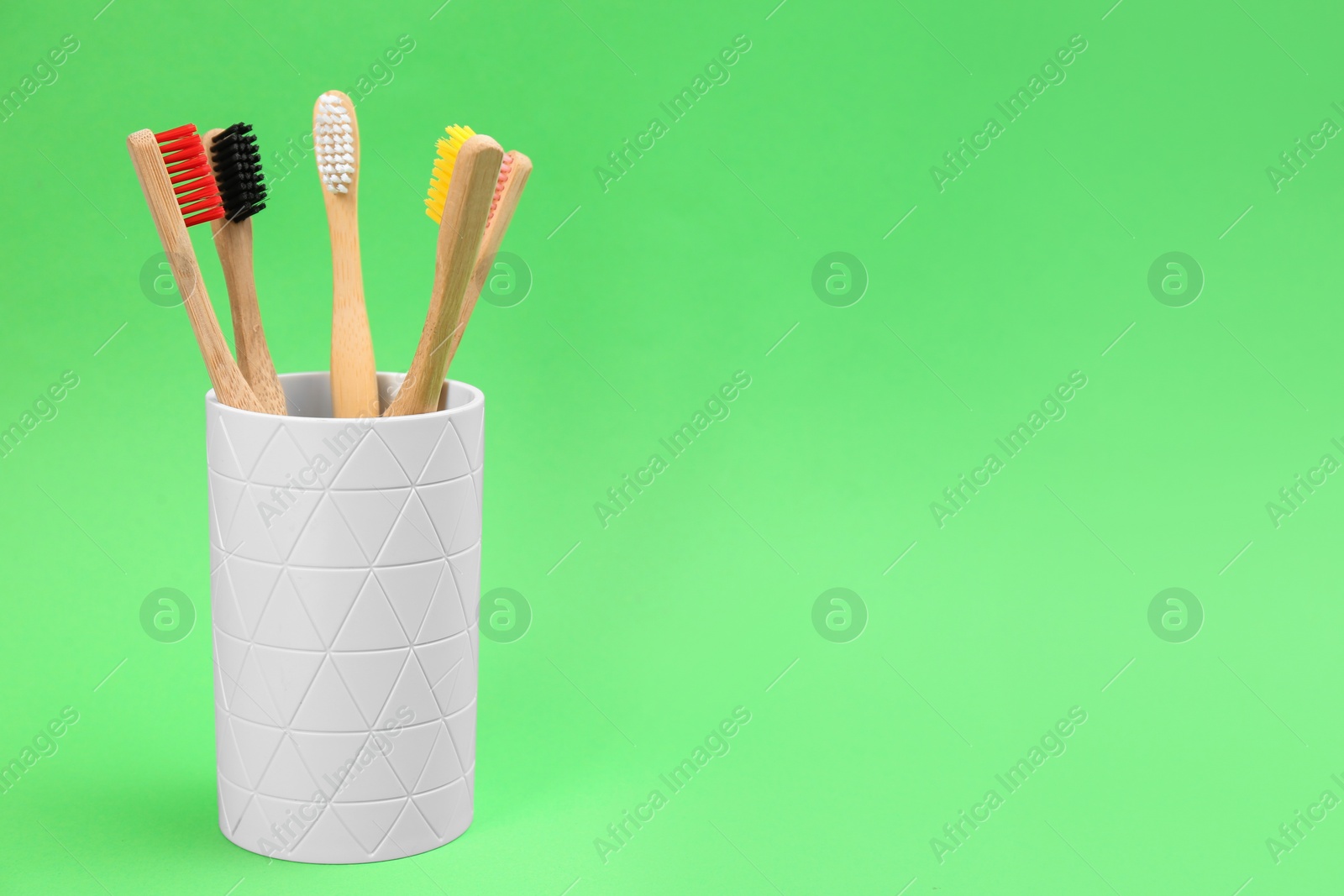 Photo of Bamboo toothbrushes in holder on green background, space for text