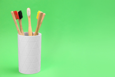 Bamboo toothbrushes in holder on green background, space for text