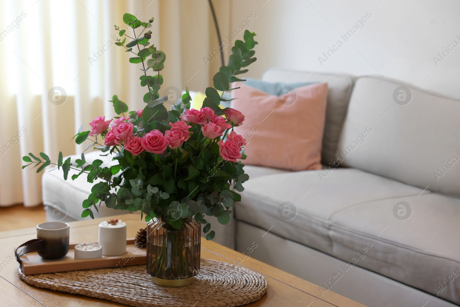 Photo of Beautiful bouquet of roses and eucalyptus branches in vase near candles on table at home. Space for text