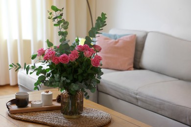 Beautiful bouquet of roses and eucalyptus branches in vase near candles on table at home. Space for text