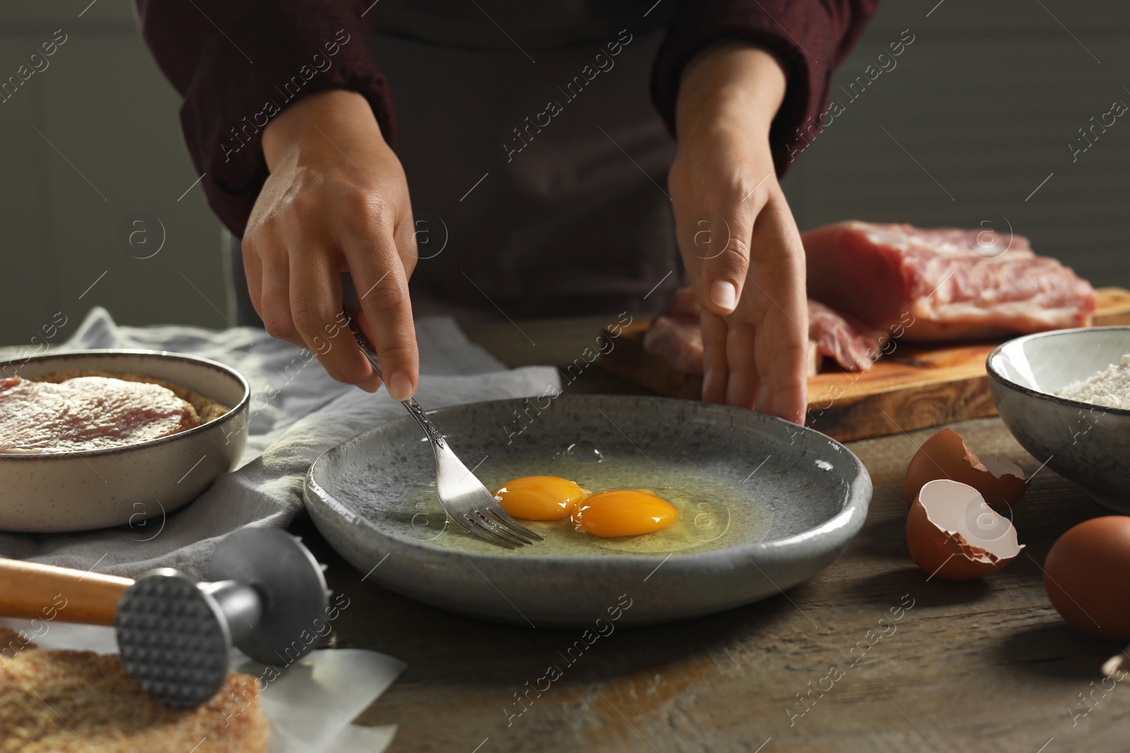 Photo of Woman cooking schnitzel at wooden table indoors, closeup