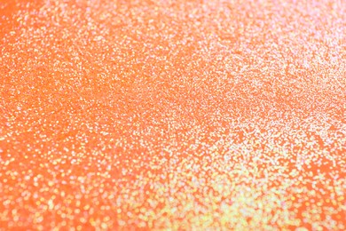 Photo of Shiny bright glitter on orange background, closeup