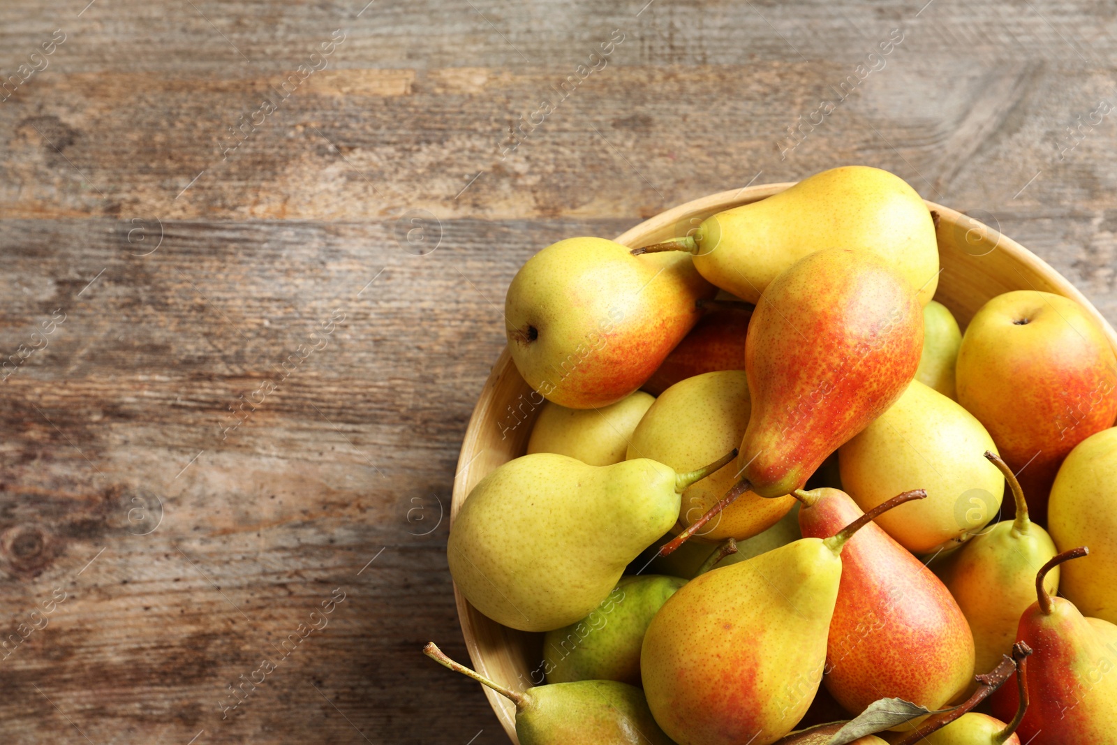 Photo of Bowl with ripe pears on wooden background, top view. Space for text