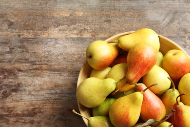 Bowl with ripe pears on wooden background, top view. Space for text