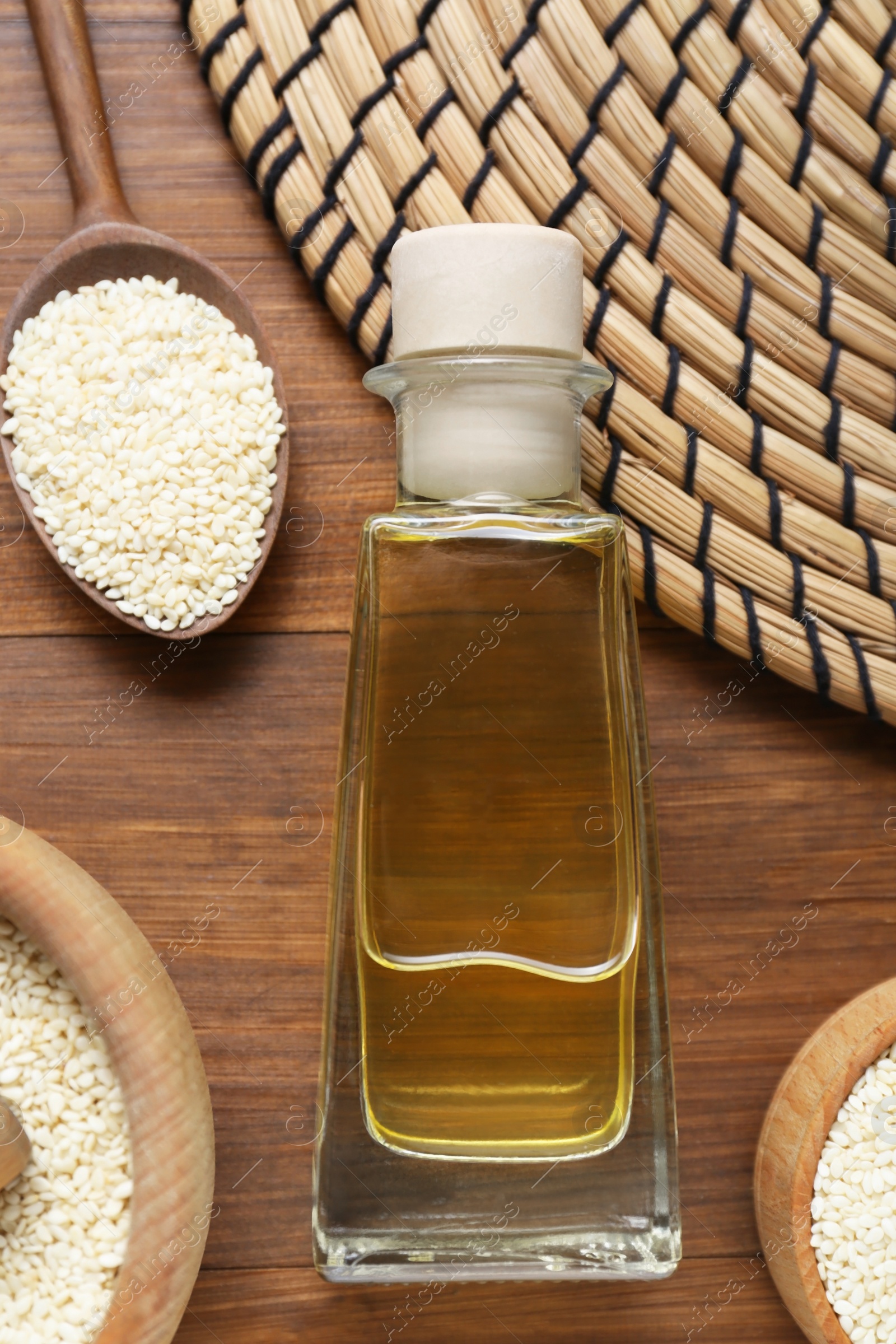 Photo of Fresh sesame oil in glass bottle and seeds on wooden table, flat lay