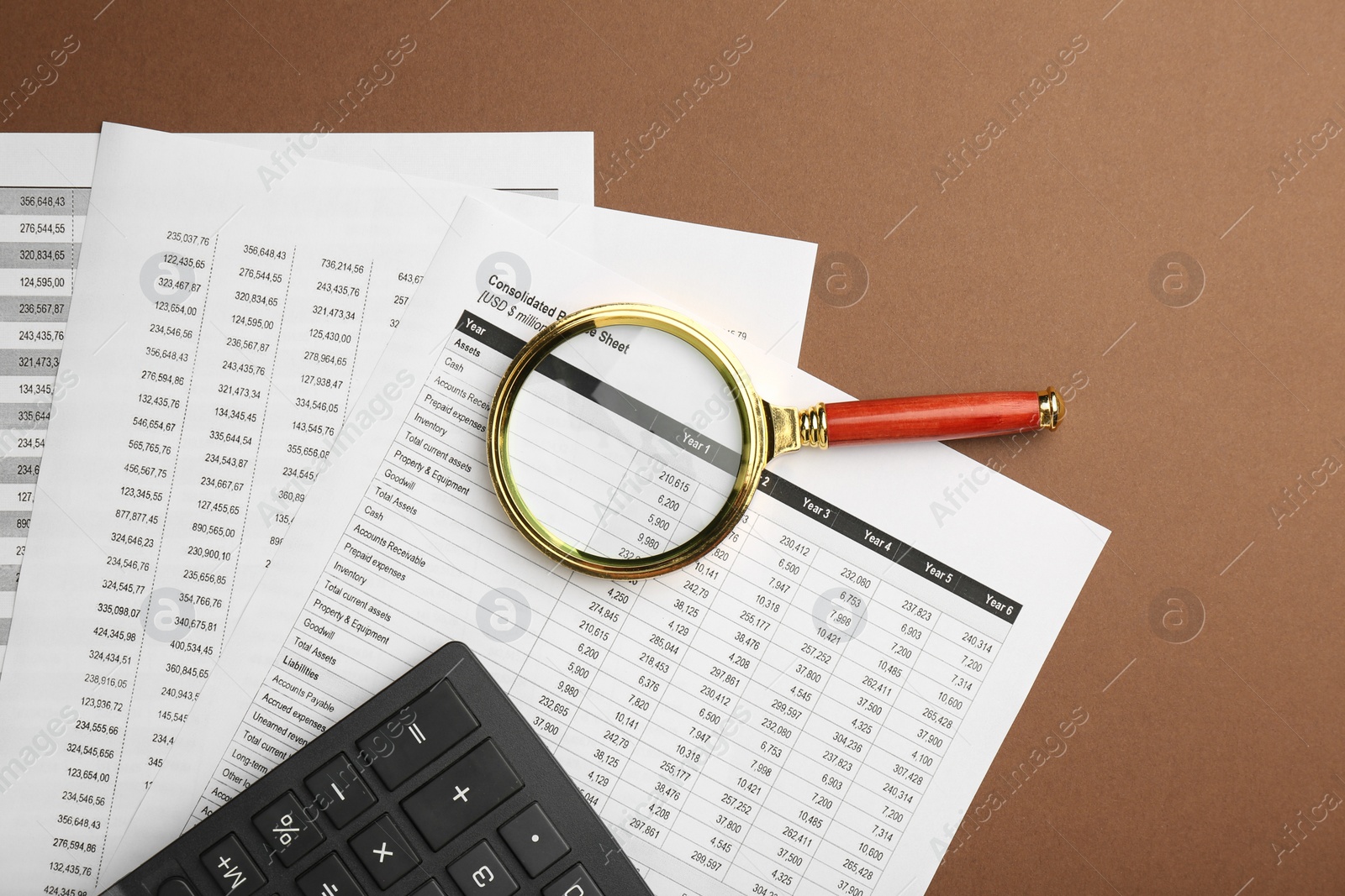 Photo of Accounting documents, magnifying glass and calculator on brown background, top view