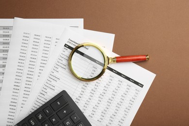 Accounting documents, magnifying glass and calculator on brown background, top view