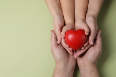 Photo of Parents and child holding red decorative heart on light green background, top view. Space for text
