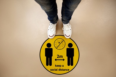 Image of Keep social distance as preventive measure during coronavirus outbreak. Yellow warning sign on floor in front of man, top view