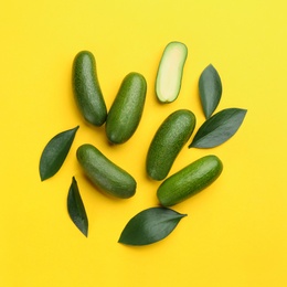 Photo of Whole and cut seedless avocados with green leaves on yellow background, flat lay